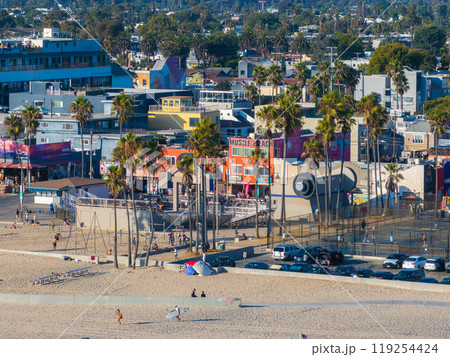 Venice Beach in Los Angeles features the iconic Muscle Beach gym, sandy shores, colorful buildings, and palm trees, capturing a lively atmosphere. 119254424