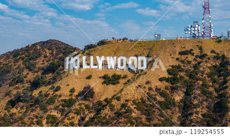 The iconic Hollywood Sign is displayed on rugged hills in Los Angeles, California, with communication towers and a partly cloudy sky in the background. 119254555