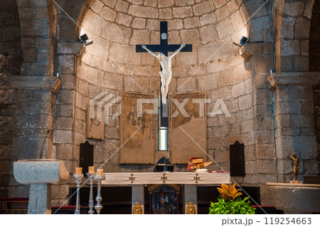 Explore the serene interior of a traditional Sardinian church, featuring a stone altar with a crucifix, framed artworks, and silver candlesticks. 119254663