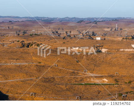 A vast desert landscape in California features numerous oil rigs amidst rolling hills. The scene includes power lines and small structures under a clear sky. A vast desert landscape in California features numerous oil rigs amidst rolling hills. The scene includes power lines and small structures under a clear sky. 119254702