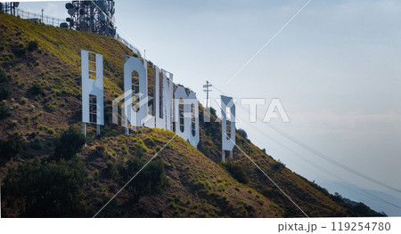 The Hollywood Sign is partially obscured on Los Angeles hills, surrounded by grassy terrain and a clear sky, with communication towers visible. The Hollywood Sign is partially obscured on Los Angeles hills, surrounded by grassy terrain and a clear sky, with communication towers visible. 119254780