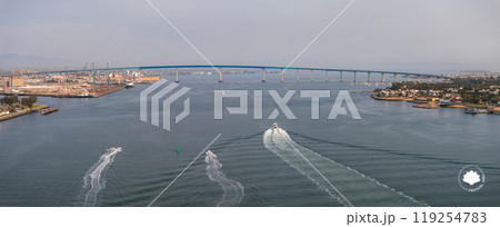 The San Diego Coronado Bridge spans the bay, with boats creating trails. Industrial areas and shipyards are on the left, greenery and urban areas on the right. The San Diego Coronado Bridge spans the bay, with boats creating trails. Industrial areas and shipyards are on the left, greenery and urban areas on the right. 119254783