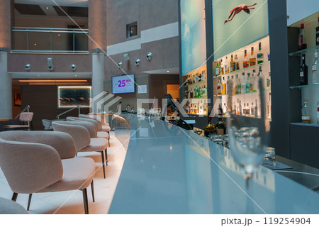 Modern bar in a Sardinian luxury hotel featuring plush seating, illuminated bottle display, and unique diving artwork, creating a sophisticated ambiance. 119254904
