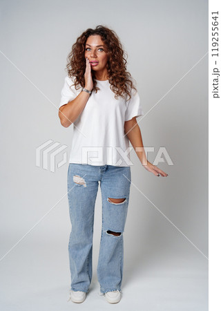 Surprised woman expressing strong emotions with wide eyes and raised hands, studio setting 119255641