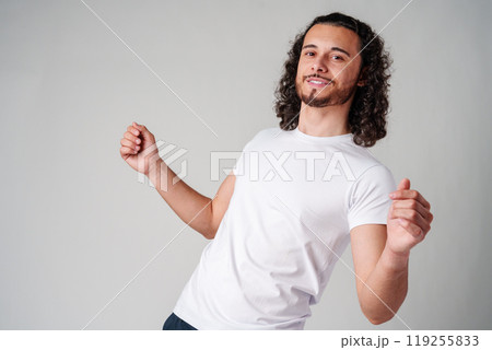 Cheerful man with curly hair joyfully celebrating indoors while wearing a casual outfit in studio Cheerful man with curly hair joyfully celebrating indoors while wearing a casual outfit in studio 119255833
