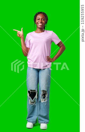 A young girl stands confidently pointing to the right against a bright green backdrop A young girl stands confidently pointing to the right against a bright green backdrop 119255955