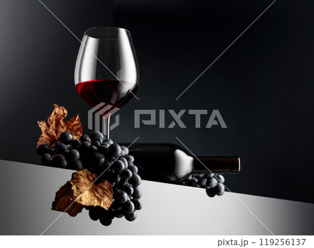 Red wine and blue grapes with dried up vine leaves on a dark background. 119256137