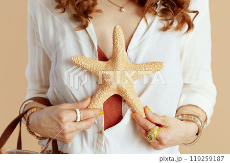 Trendy woman in blouse and shorts with sea star on beige 119259187