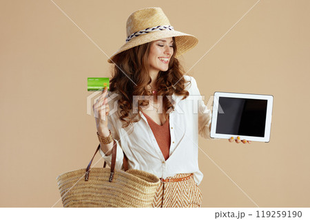 happy woman in blouse and shorts showing tablet PC on beige 119259190