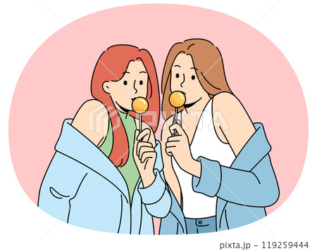 Two women with chupa chups in hands dressed in fashionable seductive clothes eat lollipops Two women with chupa chups in hands dressed in fashionable seductive clothes eat lollipops 119259444