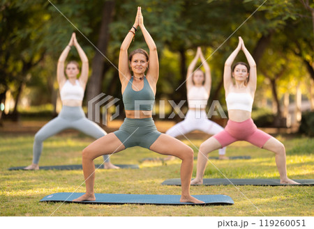 Yoga lesson visitors girls perform utkata konasana in park Yoga lesson visitors girls perform utkata konasana in park 119260051