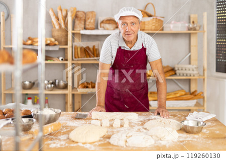 Elderly baker shapes raw dough into baguette Elderly baker shapes raw dough into baguette 119260130