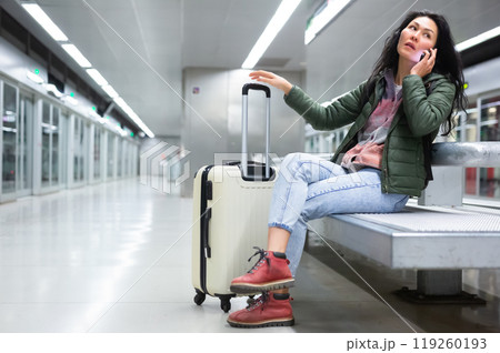 Positive asian woman talking on mobile phone while waiting for subway train at station 119260193
