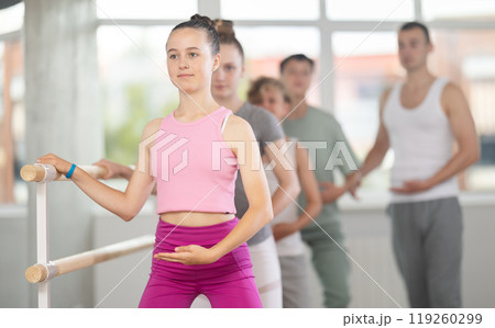 Teenagers doing ballet at group training session in the studio performs demi plie near the ballet barre, standing in ballet stance 119260299