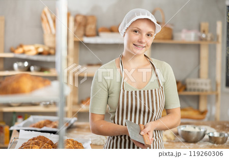 Young female baker standing with dough scraper in bakery 119260306