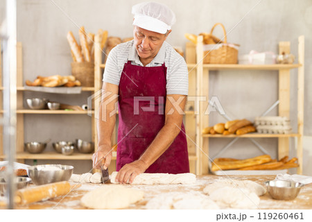 Elderly baker shapes raw dough into baguette Elderly baker shapes raw dough into baguette 119260461