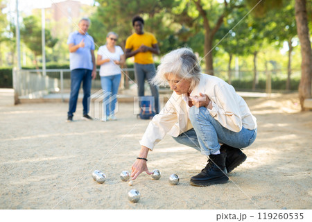 Multiracial mature adult people measuring distance between balls in petanque game outside in a park 119260535