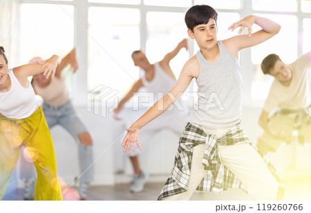 Teen guy together with group of teenage friends, learn to dance hip hop in choreographic hall. Teen guy together with group of teenage friends, learn to dance hip hop in choreographic hall. 119260766