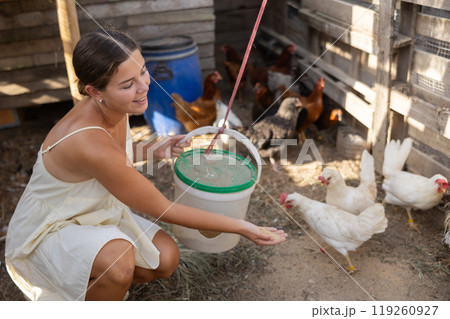 Young woman feeding chickens in henhouse Young woman feeding chickens in henhouse 119260927