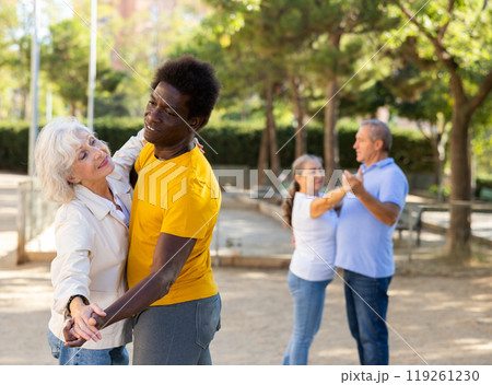 Happy positive mature multinational pensioners spending time together and dancing in pairs outdoors 119261230