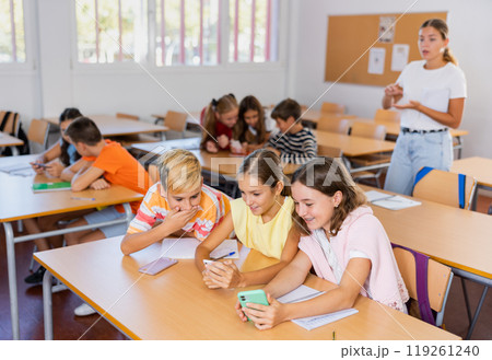 Schoolchildren use mobile phones at the lesson in classroom 119261240