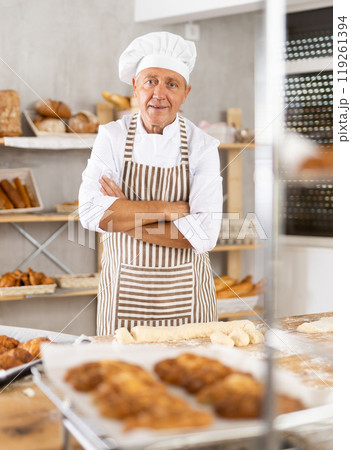 Smiling elderly baker standing with crossed arm in bakery 119261394