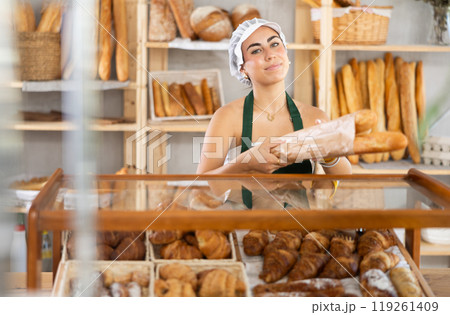 Young saleswoman holds out baguettes in paper bag in bakery Young saleswoman holds out baguettes in paper bag in bakery 119261409