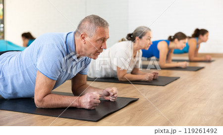 Class of male and women of different ages standing in plank on elbows during Pilates training together in gym 119261492