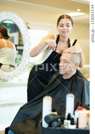 Young female hairdresser working with scissors and comb with mature man Young female hairdresser working with scissors and comb with mature man 119261534