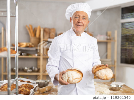 Successful senior baker holding freshly baked bread Successful senior baker holding freshly baked bread 119261540