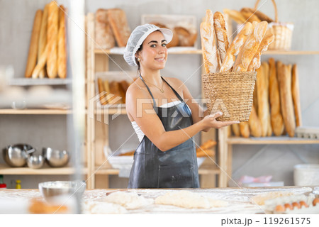 Young saleswoman displays baguettes in wicker basket Young saleswoman displays baguettes in wicker basket 119261575