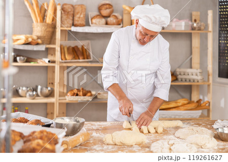 Professional elderly baker slicing dough at floured table Professional elderly baker slicing dough at floured table 119261627