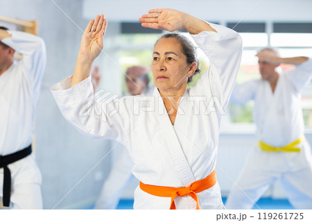 Old woman attendee of karate classes practicing kata standing in row with others 119261725