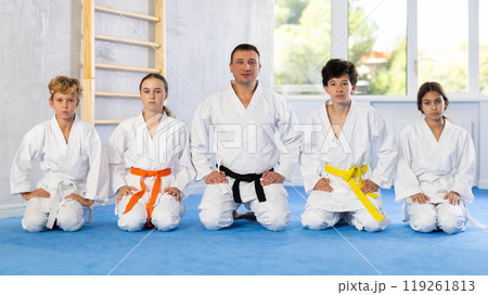 Children in white kimono sitting on knees on tatami in sport gym Children in white kimono sitting on knees on tatami in sport gym 119261813