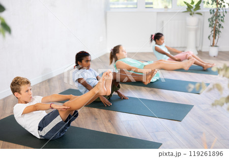 Girls and boys doing abdominal crunches with outstretched arms to strengthen abs and core muscles during group yoga class in studio Girls and boys doing abdominal crunches with outstretched arms to strengthen abs and core muscles during group yoga class in studio 119261896