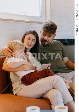 Family spending quality time together on couch, engaged with a tablet for an intimate bonding moment Family spending quality time together on couch, engaged with a tablet for an intimate bonding moment 119261898