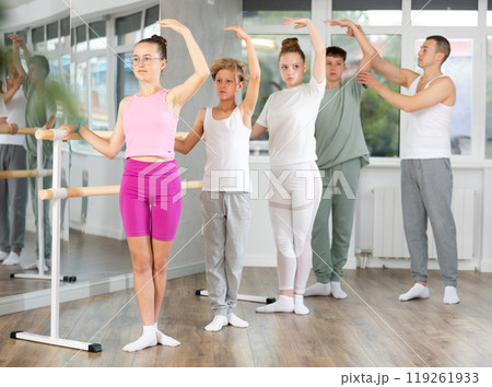 Group of teenagers stand in third position near ballet barre during group training in dance studio 119261933