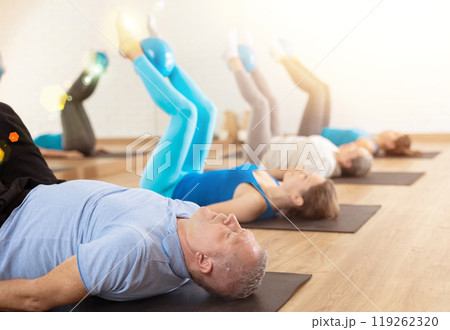 Class of people of different ages holding balls between legs and pushing press during Pilates training in studio 119262320