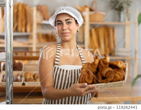 Young saleswoman displays croissants in square wicker basket 119262441