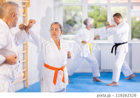 Old woman attendee of karate classes fighting with her opponent in sports hall Old woman attendee of karate classes fighting with her opponent in sports hall 119262526
