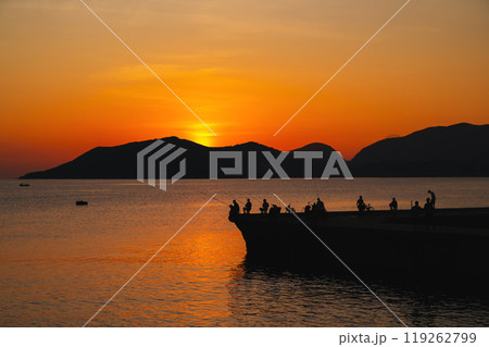 Silhouettes of fishermen with fishing rods fishing on a pier in the sea in morning at dawn in summer 119262799