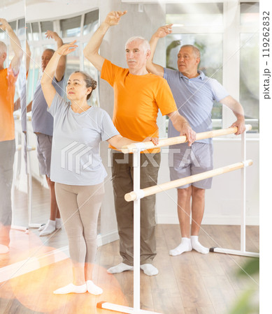 Group of positive elderly women and men engaged in classical ballet in dance studio performs exercise standing in 3rd position of ballet stance 119262832