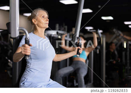 Elderly woman exercising chest muscles on butterfly machine 119262833
