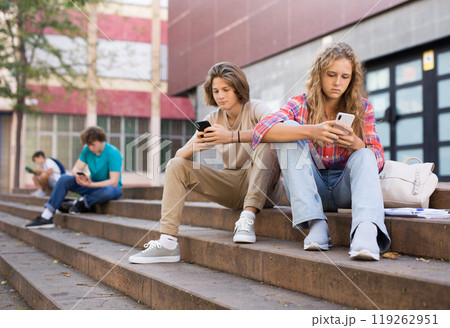 Teenage friends boy and girl holding phones and browsing Teenage friends boy and girl holding phones and browsing 119262951