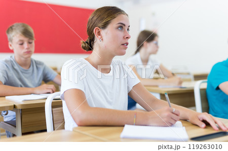 Girl high school student listening to teacher and making notes during lesson 119263010