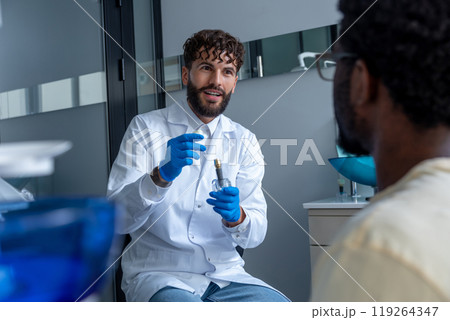 Young man dentist providing consultation in dental office for unrecognizable patient 119264347