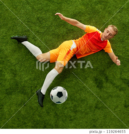 As he takes fall, soccer player's attention remains on football. Persistence and dedication during game. Aerial view. As he takes fall, soccer player's attention remains on football. Persistence and dedication during game. Aerial view. 119264655