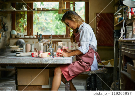 Female artist decorating and painting handmade ceramic clay cup at her creative workshop Female artist decorating and painting handmade ceramic clay cup at her creative workshop 119265957