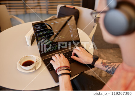 Over shoulder shot of male software developer writing code on laptop sitting at cafe table with cup of coffee at hand during coffee break or lunch, copy space Over shoulder shot of male software developer writing code on laptop sitting at cafe table with cup of coffee at hand during coffee break or lunch, copy space 119267390