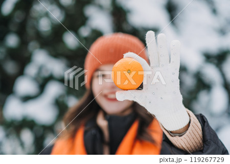 Close-up of woman holding an orange in a snowy outdoor scene. Winter immunity, fresh citrus, healthy living during cold season 119267729